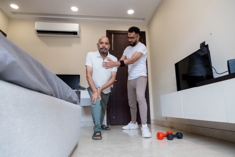 Senior Man Assisted by Caregiver During Home Physiotherapy Session