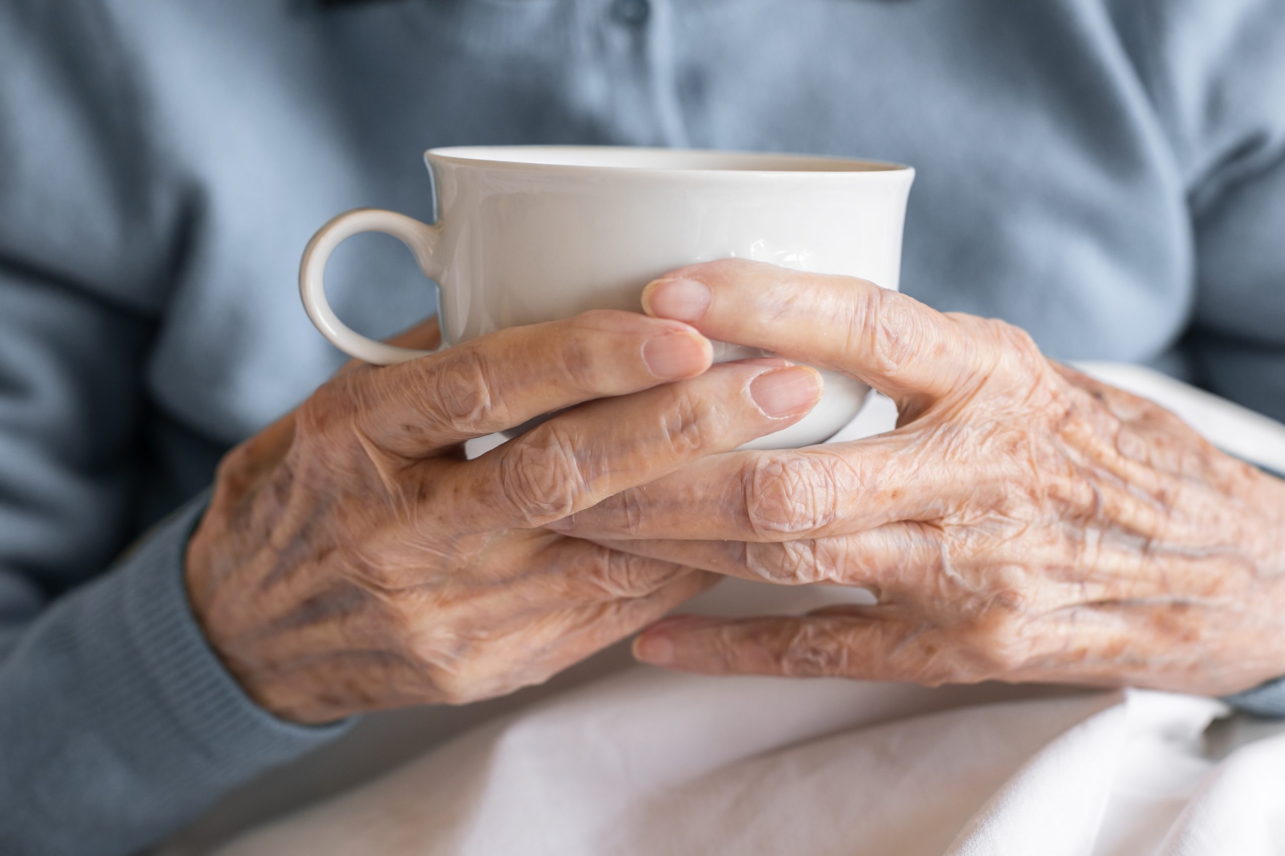 Older adult's hands resting around a warm cup of tea at home, managing arthritis pain