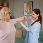 Physiotherapist helping mature adult woman with arm exercises during rehabilitation at home
