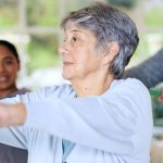 elderly client doing resistance band exercise at home with physiotherapist