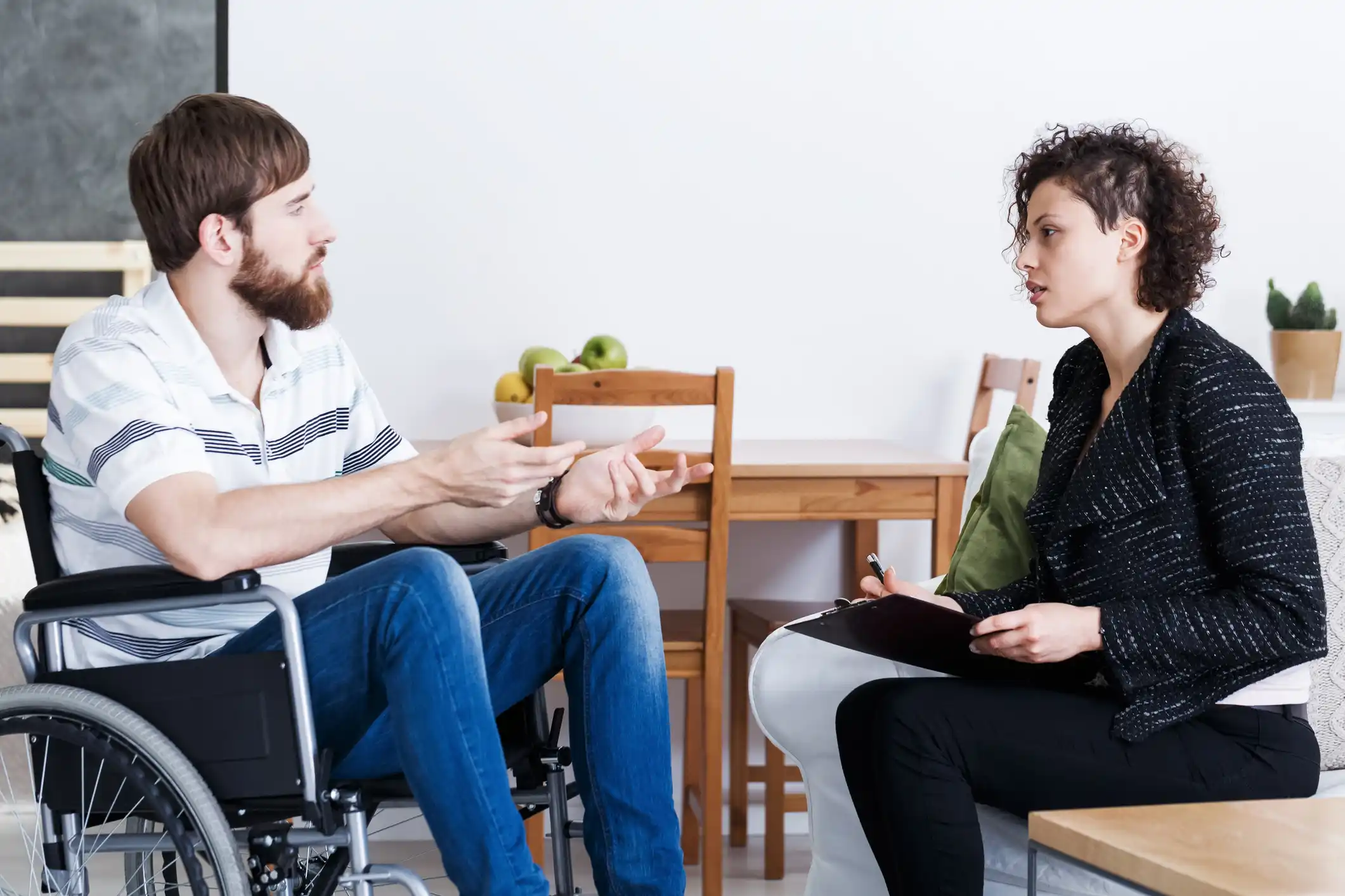 Adult wheelchair user discussing functional needs with a professional during a home consultation