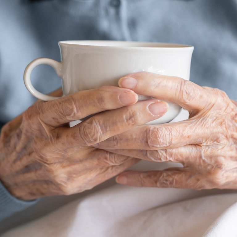 Older adult's hands resting around a warm cup of tea at home, managing arthritis pain