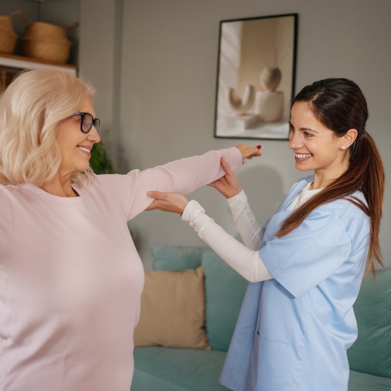Physiotherapist helping mature adult woman with arm exercises during rehabilitation at home